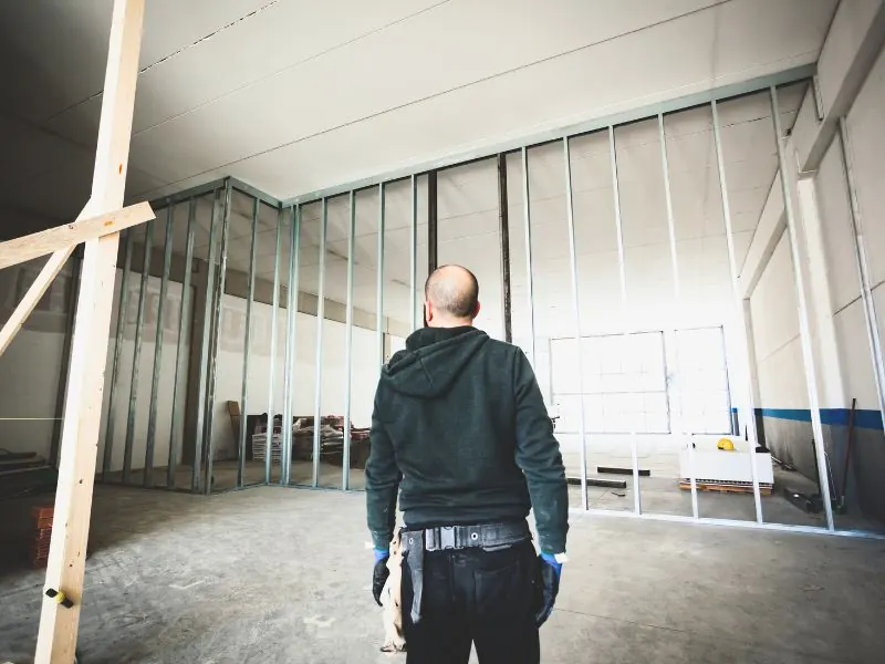 Arbeiter geht auf eine hohe Metallständerwand zu, die für den Ladenbau im Gewerbe errichtet wurde.